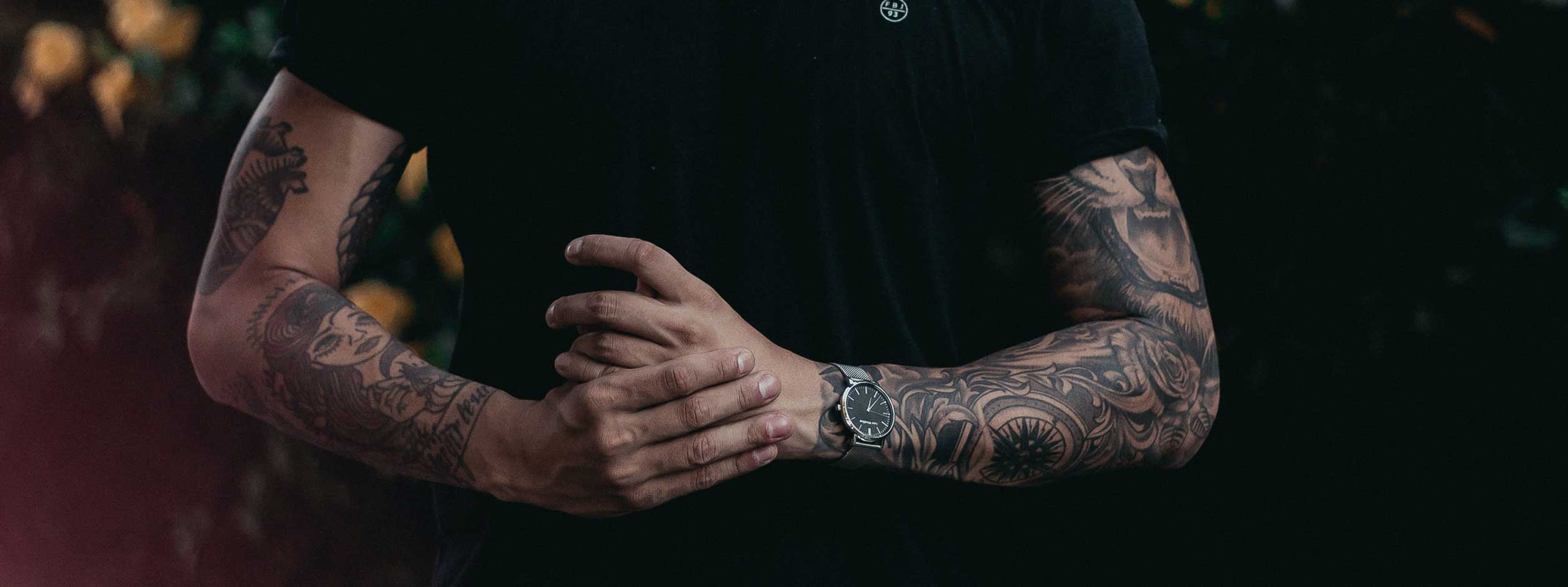 man in black t-shirt clasping hands showing fully tattooed forearms